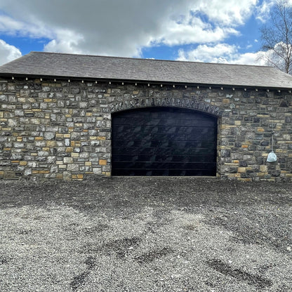 New build garage with a black door and a stone façade in Fieldstone Blend. 