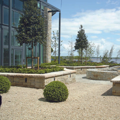 Outdoor area with low stone walls completed in Gold Donegal Quartzite Machined, greenery, and a building in the background. 