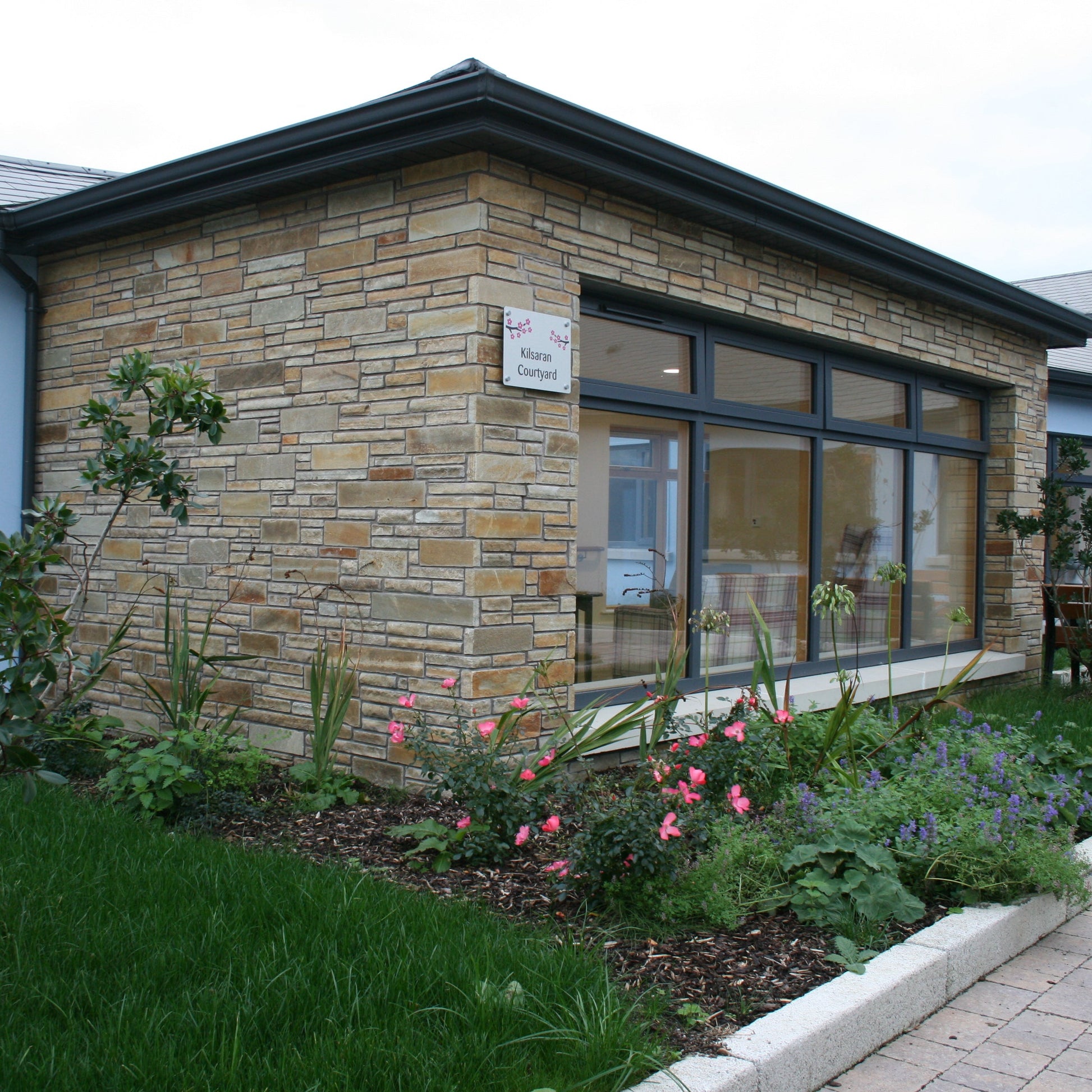 Building exterior with stone facade completed in Gold Donegal Quartzite Garden Walling in machined form, large windows, and garden area.