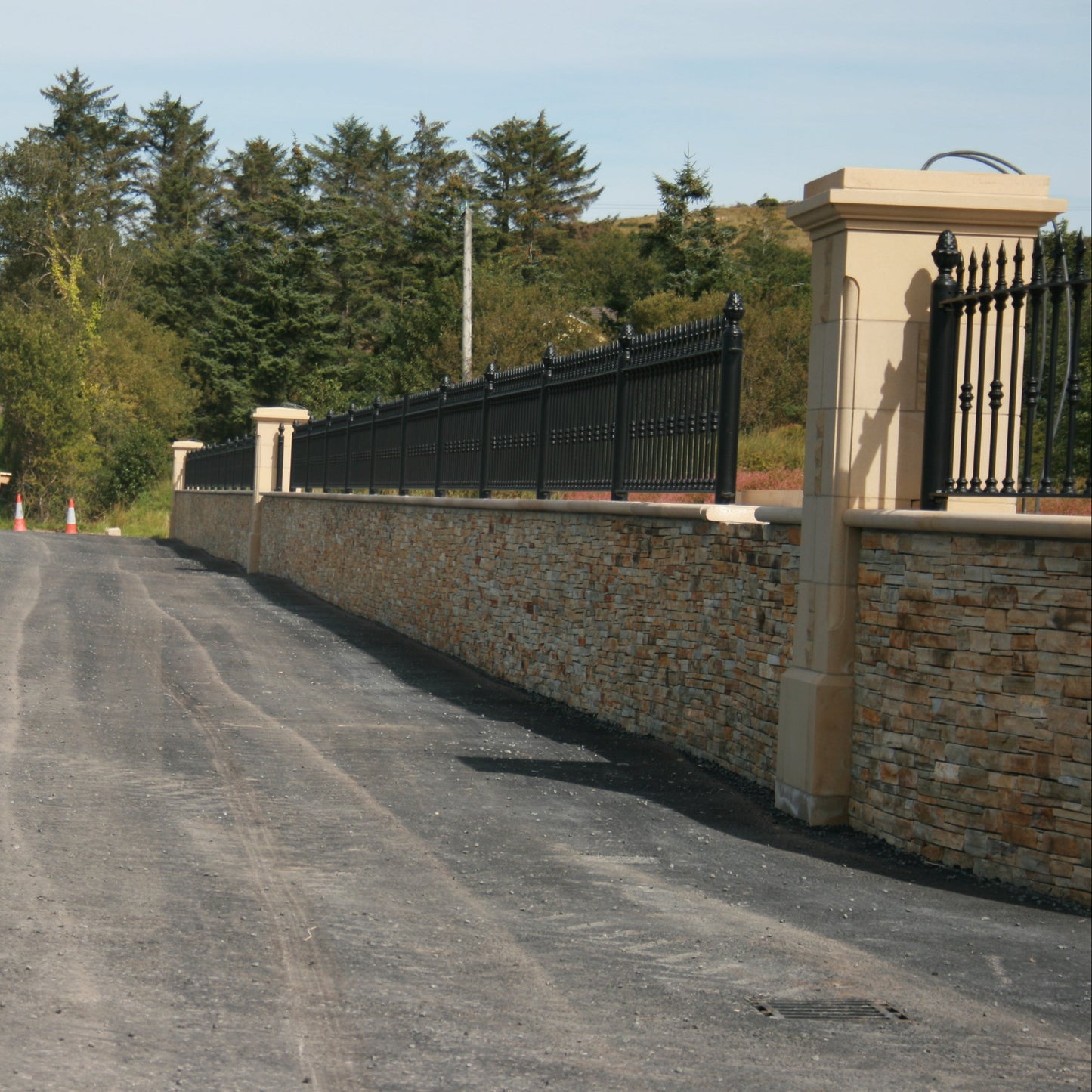 Winding road with a stone wall completed using Gold Donegal Quartzite Machined and metal gate on a clear day.