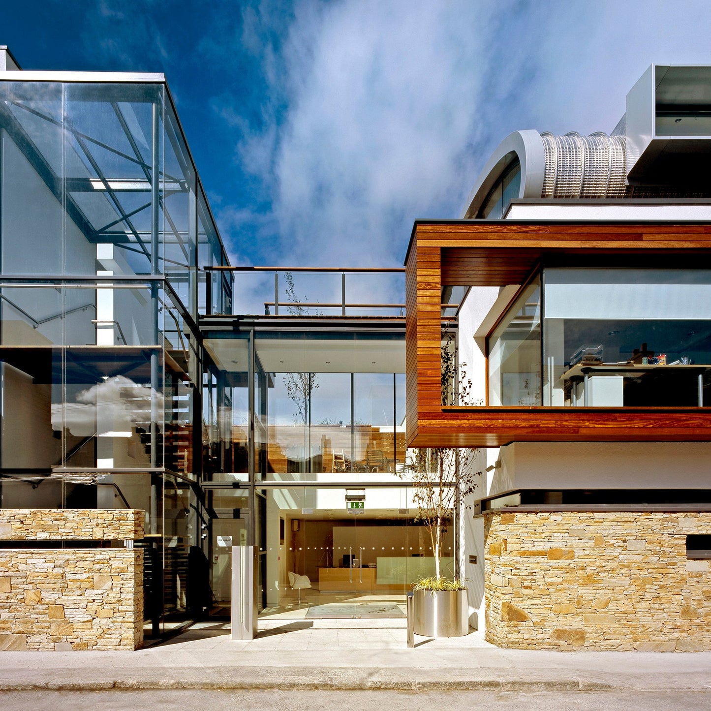 Modern building completed with Gold Donegal Quartzite Random Rubble walling stone and glass design against a blue sky.