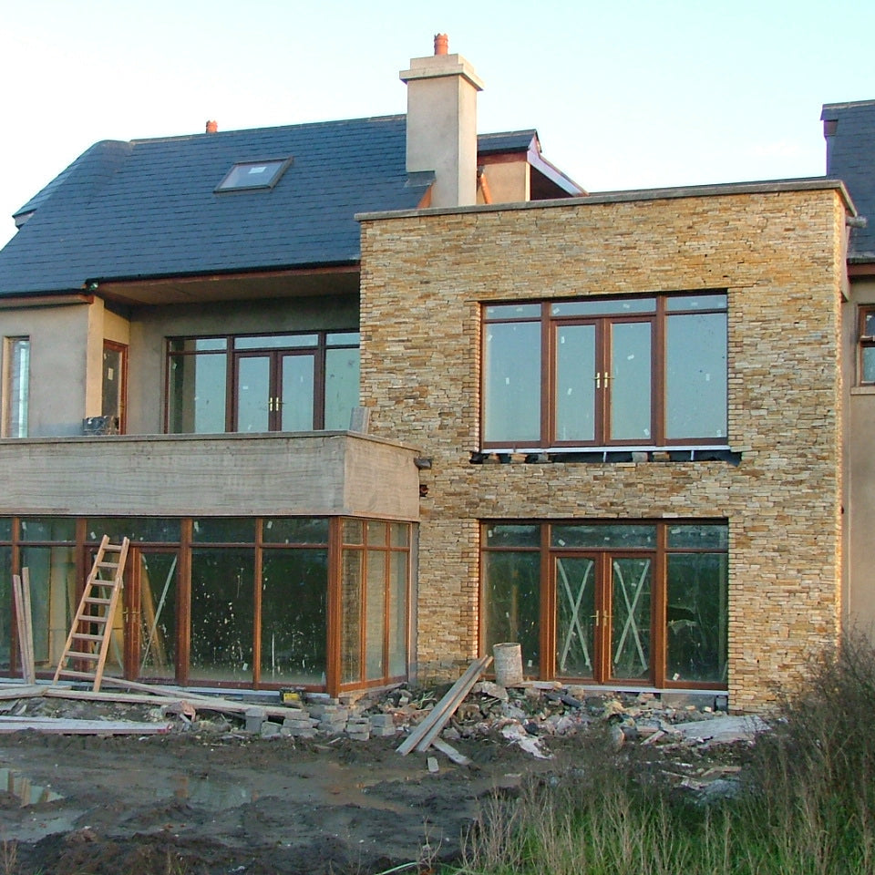 Modern house under construction with large windows and stone facade completed using our Gold Donegal Quartzite Random Rubble walling stone.