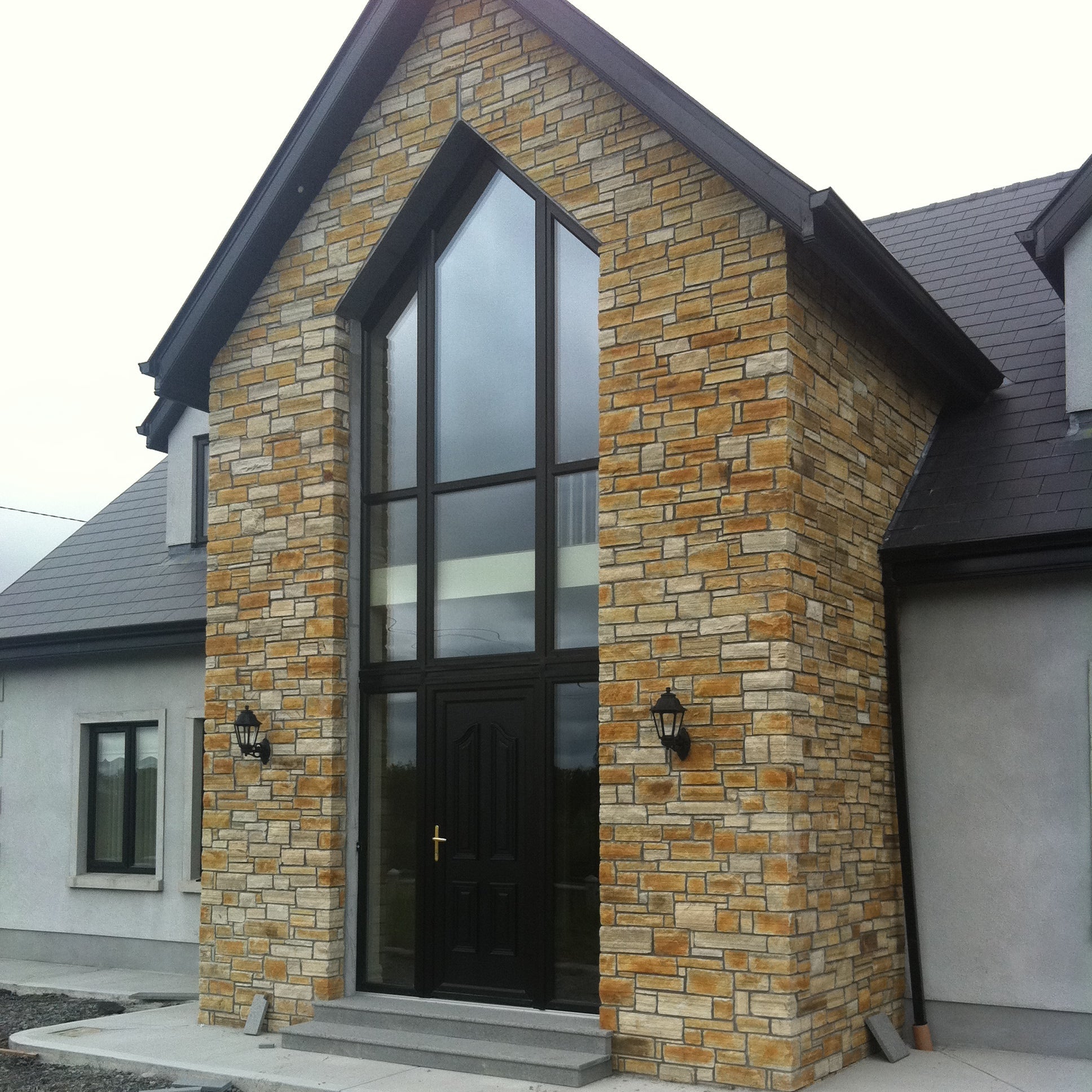 House with stone facade and large glass door. Stonework is Gold Donegal Quartzite Stoneer Cladding. 