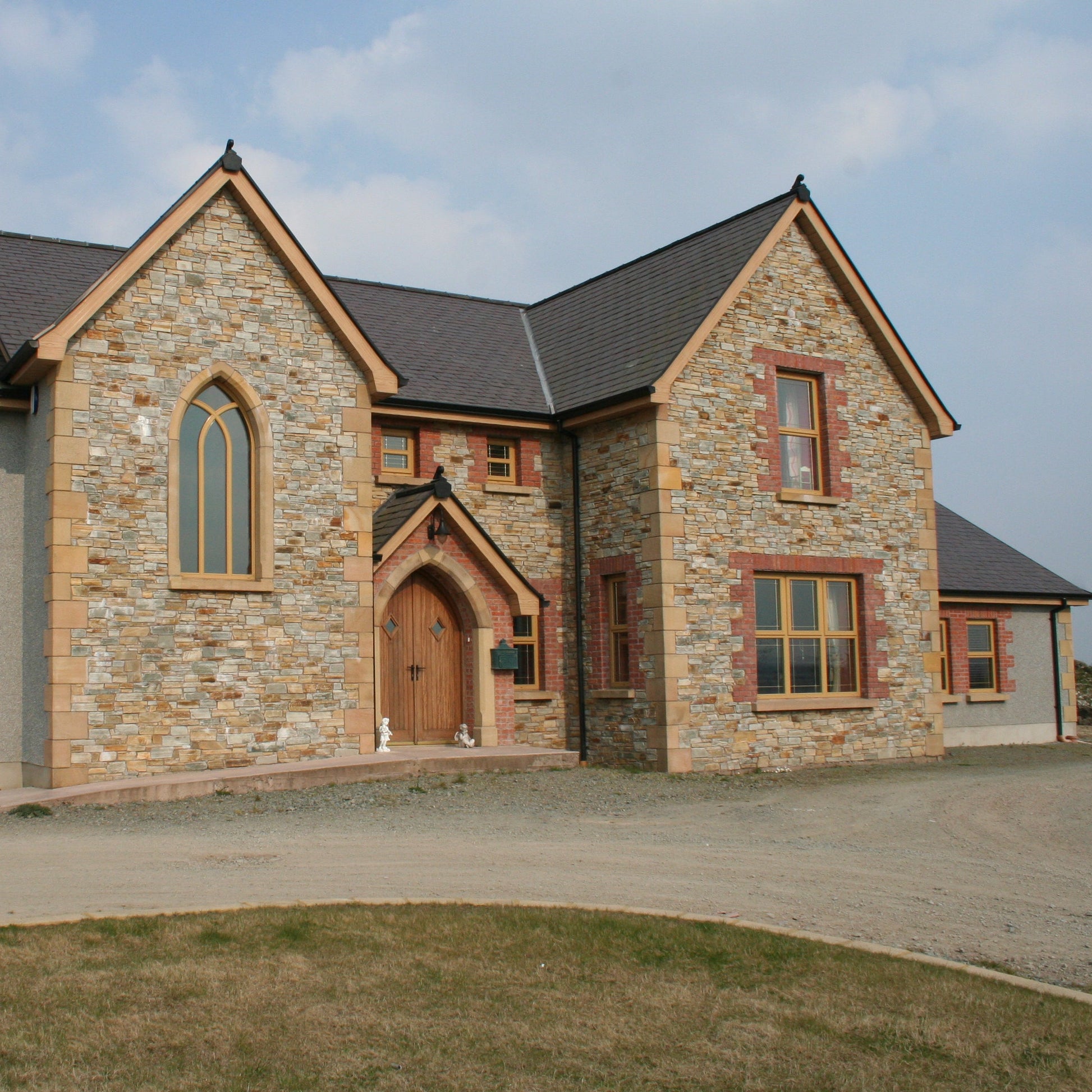 House completed using Gold Donegal Quartzite Random Rubble walling stone, architectural sandstone surrounds, quoins and red brick around the windows and front door. 