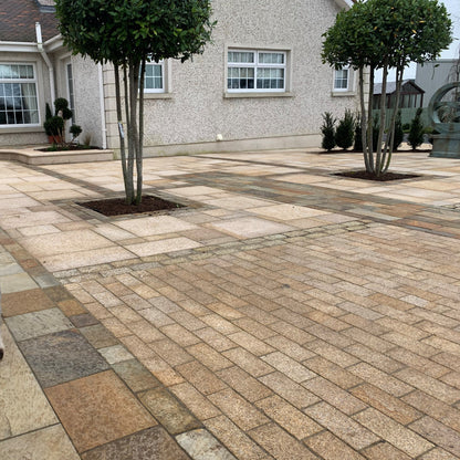 Patio area with two trees surrounded by natural stone paving in different styles and formats. In the foreground is Sawn Gold Granite Paving Cobbles in 200 x 100mm size.