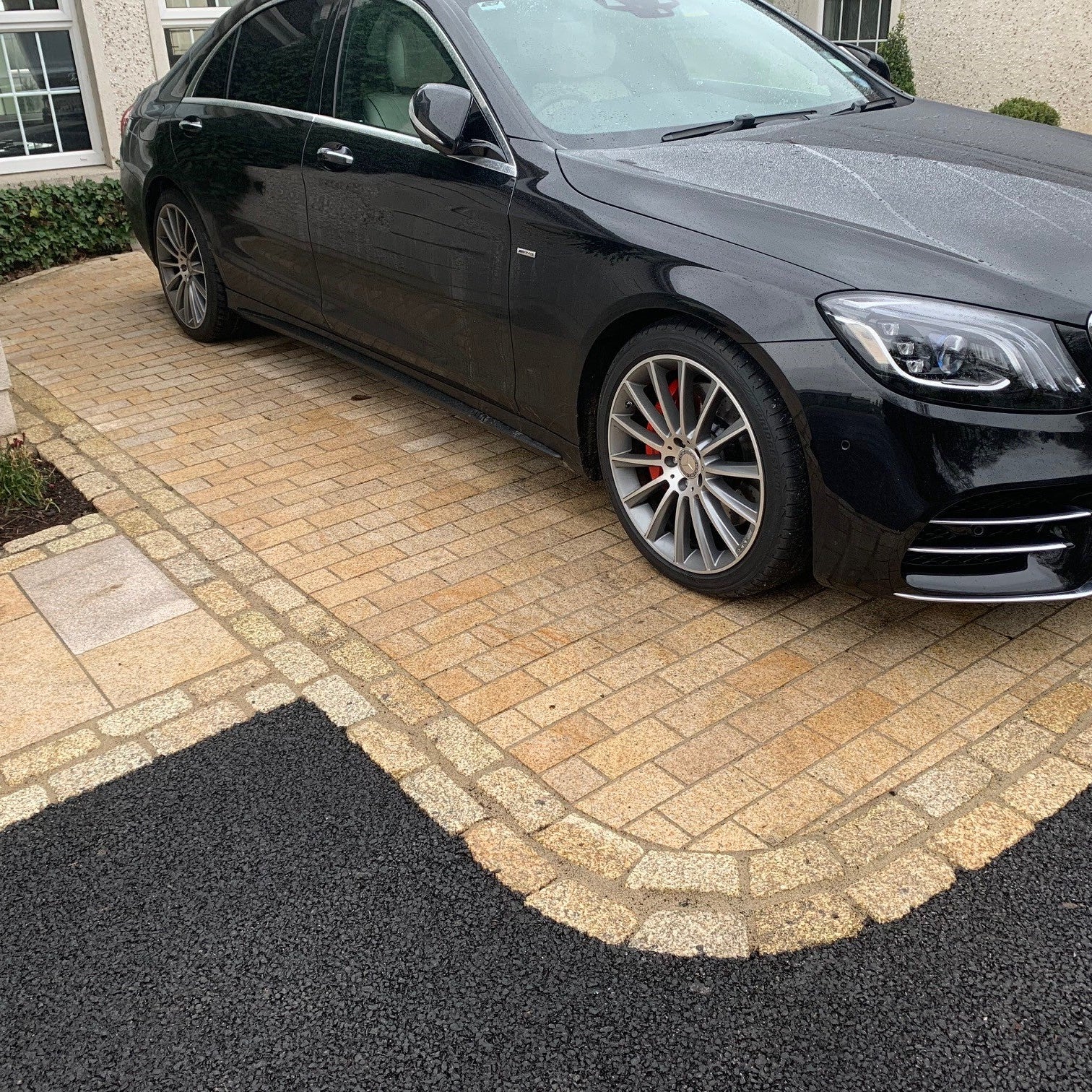 Black Mercedes-Benz car parked on a driveway featuring Sawn Gold Granite Paving Cobbles surrounded by a border of tumbled Gold Granite Cobbles. 