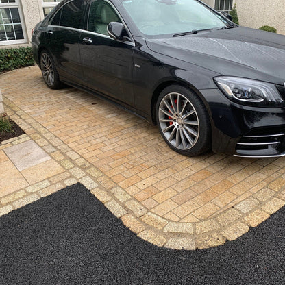 Black Mercedes-Benz car parked on a driveway featuring Sawn Gold Granite Paving Cobbles surrounded by a border of tumbled Gold Granite Cobbles. 
