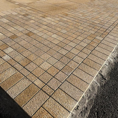 Paved patio area with a house in the background. Two cobble sizes with the outer border featuring Sawn Gold Granite in 200 x 100mm size.