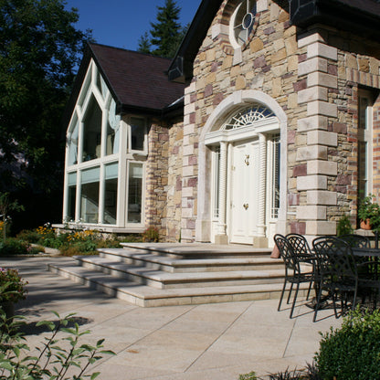 Stone house with large windows and outdoor seating area with Gold Granite Steps leading up to the front door. 