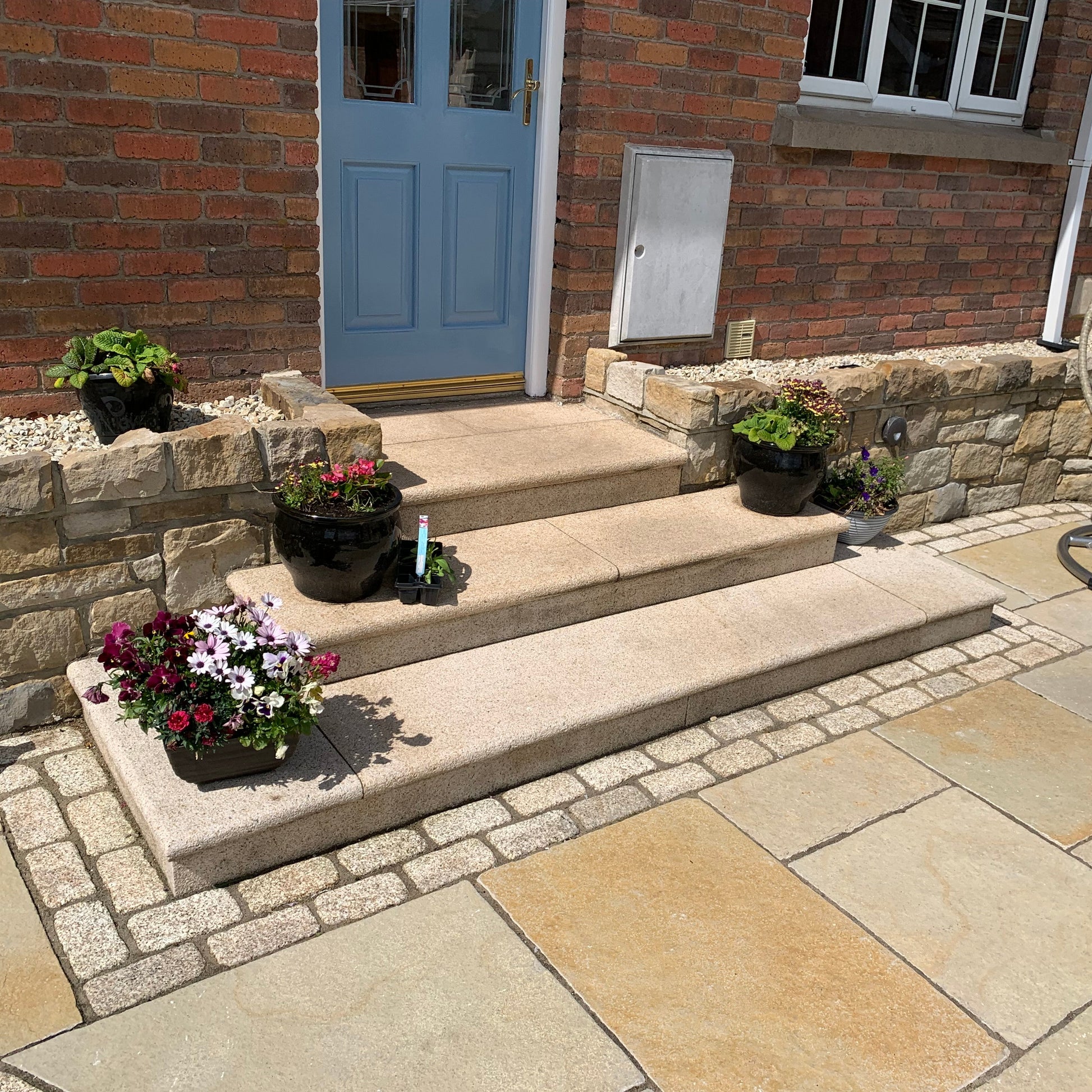 Gold Granite Steps and cobbles leading up to a blue door on a red brick house. 