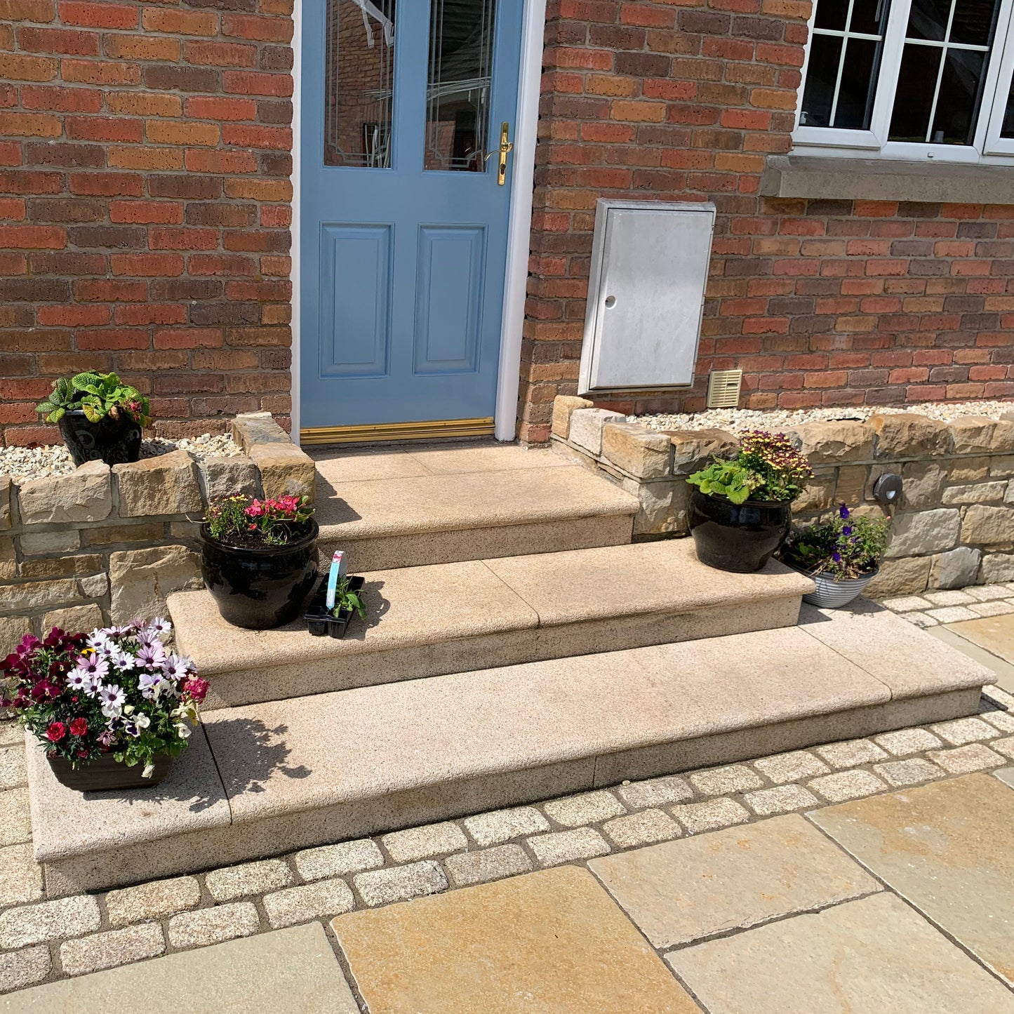 Front steps leading to a blue door with potted plants on a stone wall. Steps completed using Gold Granite Corner Steps.