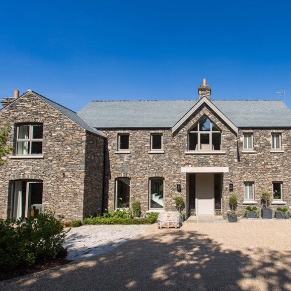 Large stone house with a clear blue sky above. House features a bespoke Gold Granite Door Lintel. 