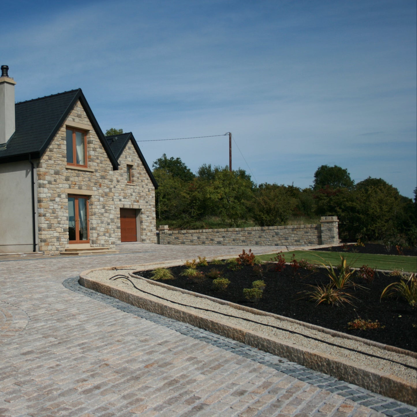 Stone house with a driveway leading up to it, surrounded by greenery. Driveway edging completed using Gold Granite Kerbs with a pineapple finish. 