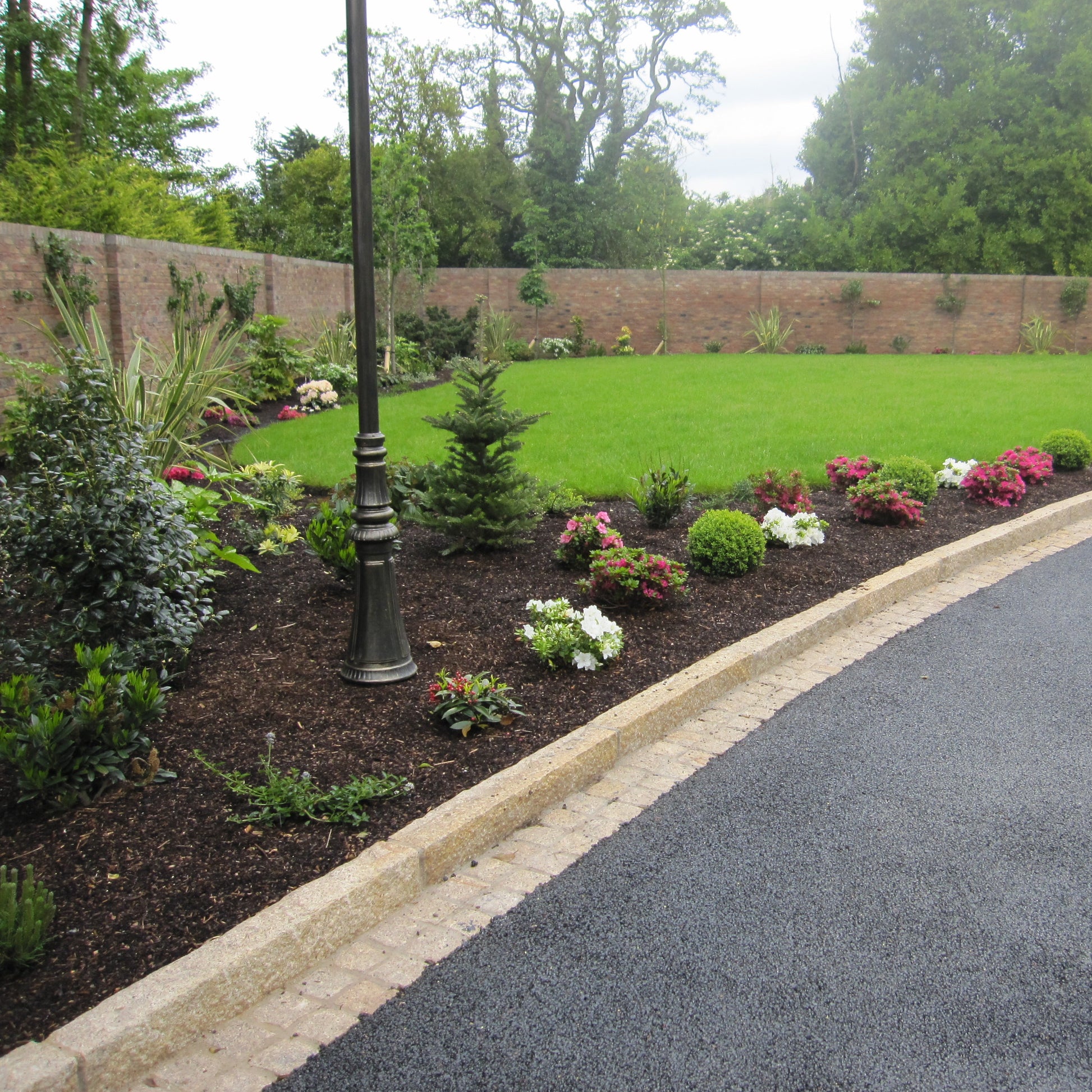 Lush garden with a well-maintained lawn, flowers, and a driveway completed using tarmac, gold granite cobbles and Gold Granite Kerbs with a pineapple finish. 