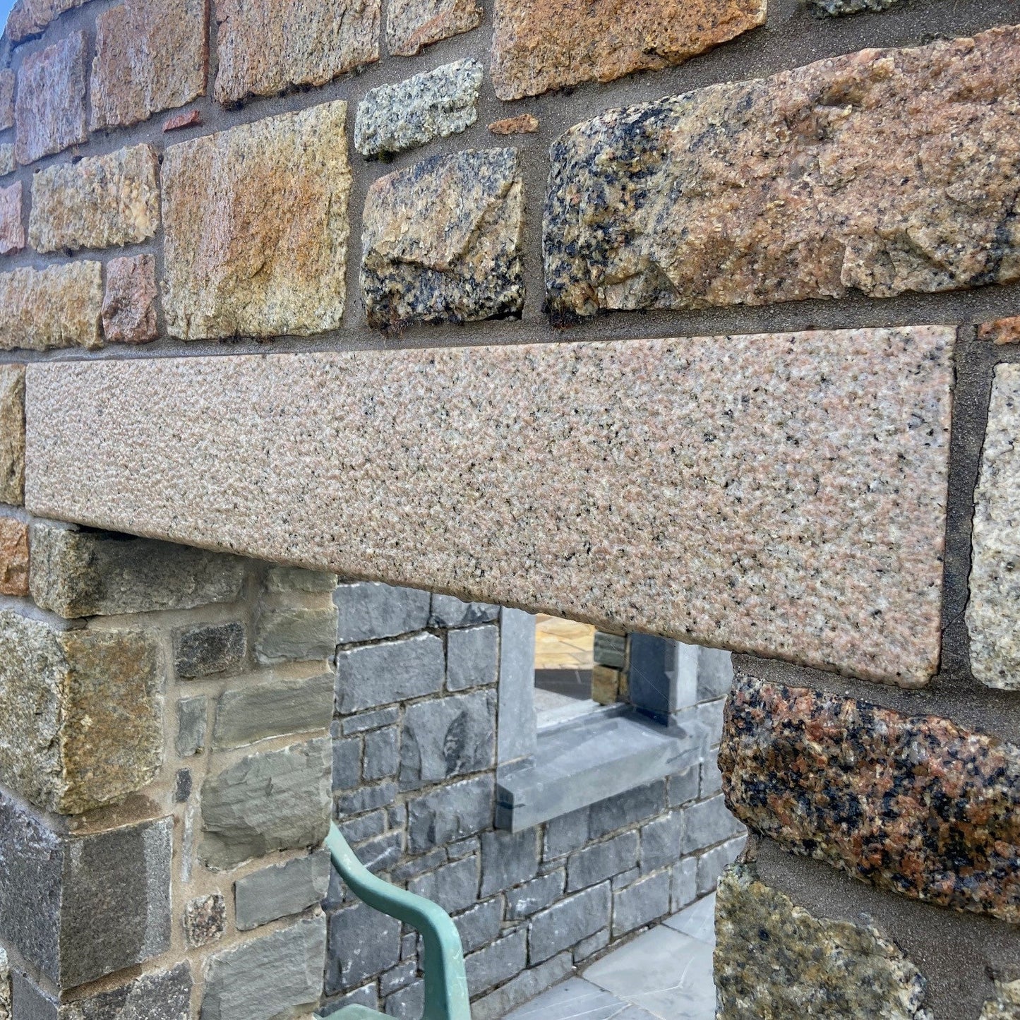 Close-up of a stone wall with various coloured stones and a bespoke gold granite lintel. 