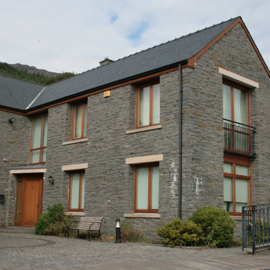Modern house with liscannor  exterior and wooden doors and windows some with bespoke Gold Granite Lintels surrounded by greenery.