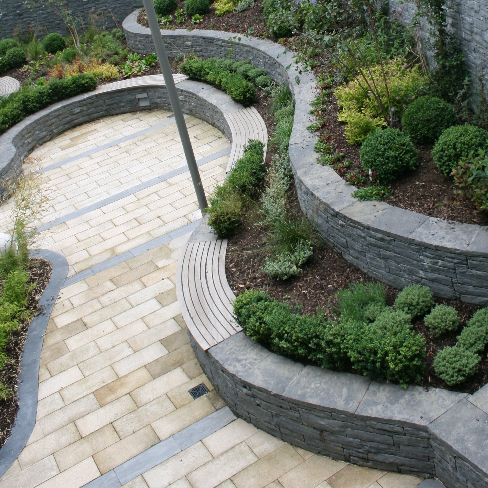 Unique garden design featuring flower beds at different levels and patio area completed using Gold Granite Paving 600 x 300mm size. 