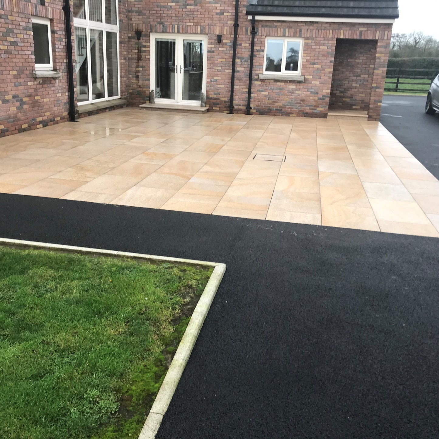 Patio area completed using Gold Granite Paving in 900 x 600mm size. Surrounded by Tarmac and garden. 