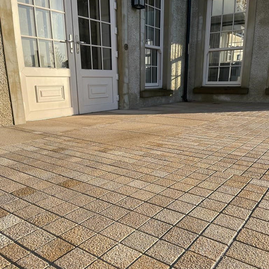 Paved patio area in front of a building with large windows. Paving features Sawn Gold Granite Cobbles with a bush hammered finish. 