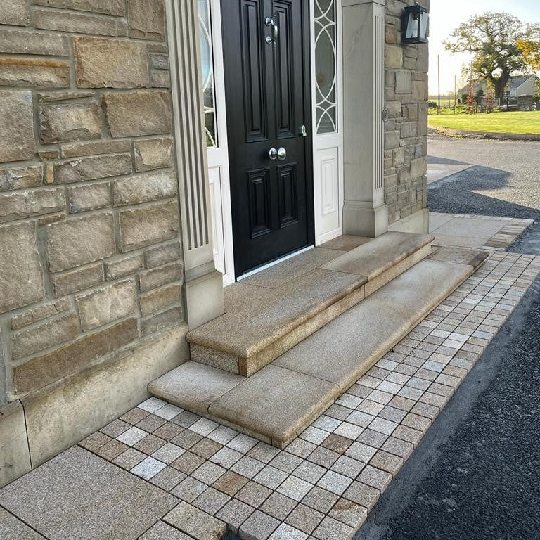 Black door with glass panels on a stone building entrance. Pathway features Sawn Gold Granite Paving Cobbles in 100 x 100mm size. 