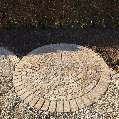A circular pattern of gold granite paving cobbles with a bush hammered surface and lightly tumbled edges installed on a bed of gravel. Inner cobbles are Gold Granite  Paving Cobbles in 100 x 100mm size. with outer circle in 200 x 100mm size. 