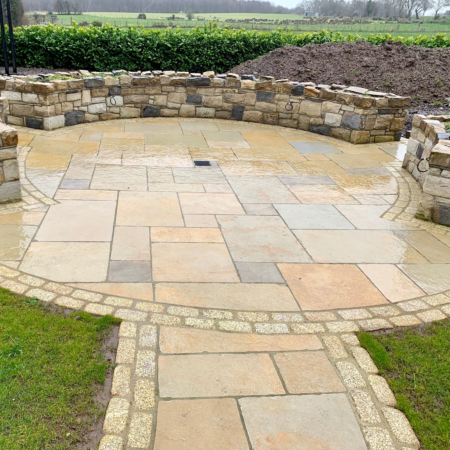 Circular patio area with stone walls completed using yellow limestone paving and double row of Gold Granite Paving Cobbles in 200 x 100mm 