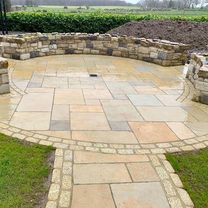 Circular patio area with stone walls completed using yellow limestone paving and double row of Gold Granite Paving Cobbles in 200 x 100mm 