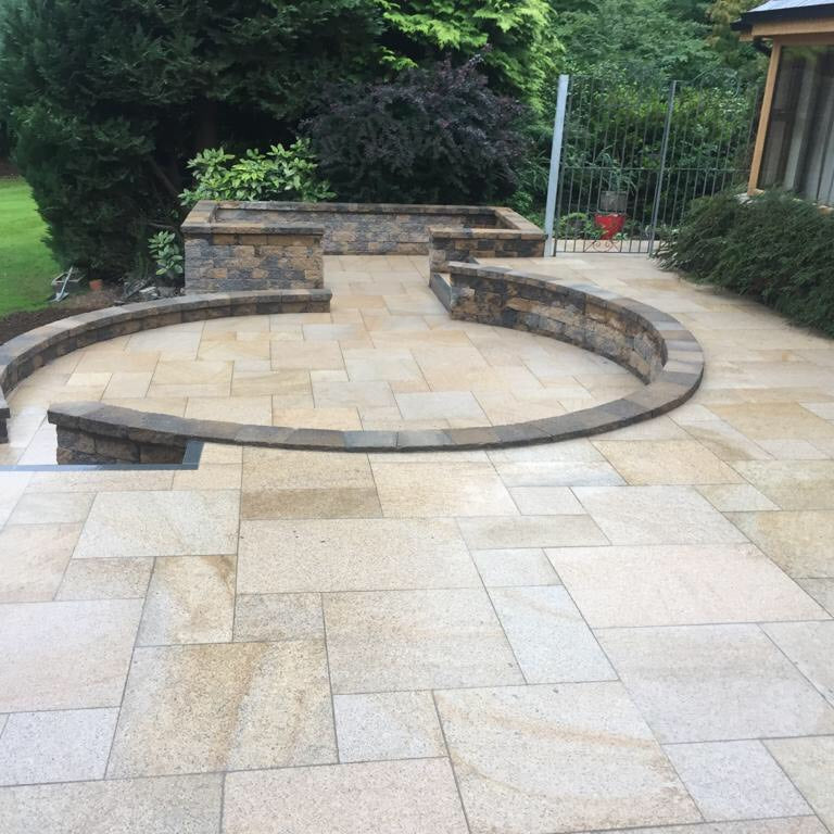 An outdoor patio area featuring Gold Granite paving in a circular pattern with a garden and house in the background.