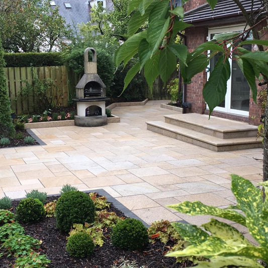 Patio with steps and BBQ surrounded by beautiful planting. Paving is Gold Granite in mixed patio pack sizes. 