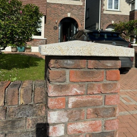 Brick house with a car parked in front, featuring a stone wall and greenery.