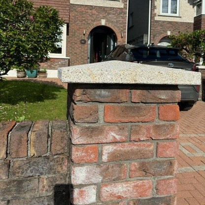 Brick house with a car parked in front, featuring a stone wall and greenery.