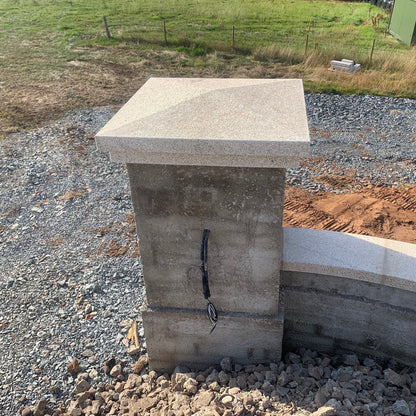 Bespoke Gold Granite Pillar and Wall Capping newly installed to concrete wall structure on a gravel surface with grass and a fence in the background. 