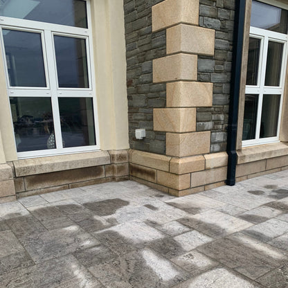 Paved patio area with stone wall and windows. Wall features bespoke Gold Granite Quoins and Plinths. 