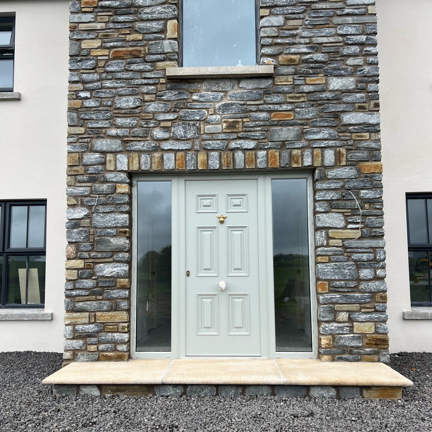 Stone façade of a new build house with a grey door and windows. Front step was completed using Gold Granite Step. 