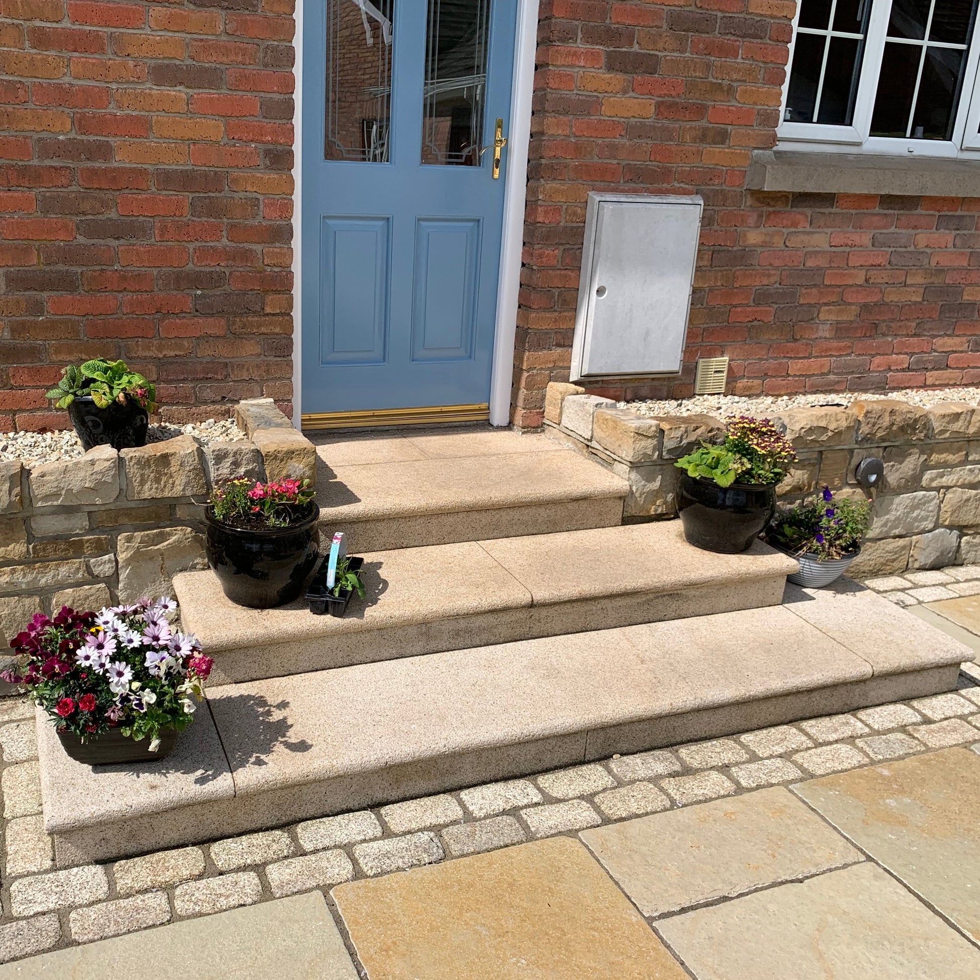 Front steps completed using Gold Granite step packs leading to a blue door with potted plants on a stone wall.