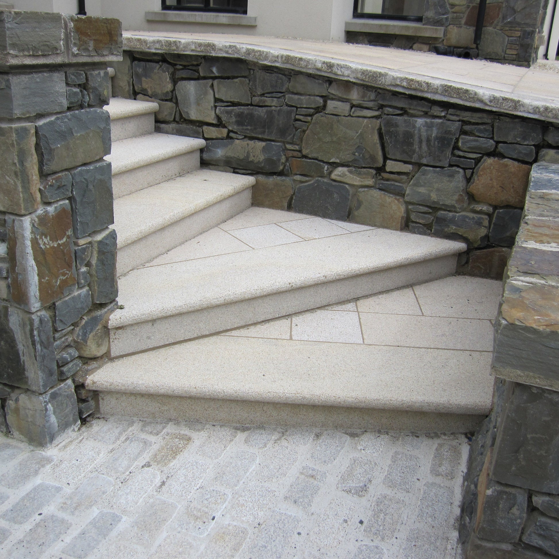 Gold Granite Step & Riser Sets leading up to a stone wall with a paved walkway.