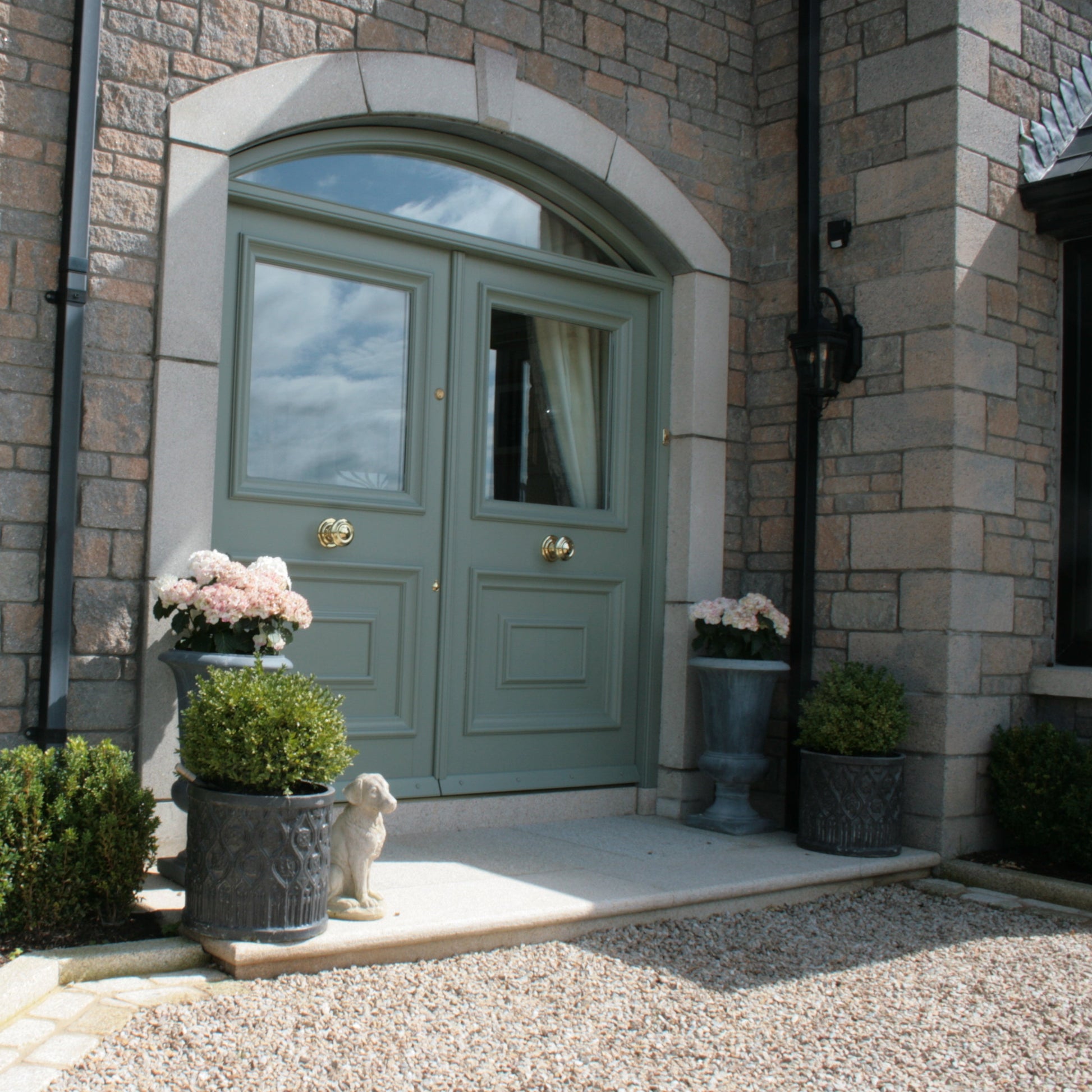 Green double door entrance of a stone building with decorative elements. Gold Granite Step Pack. 