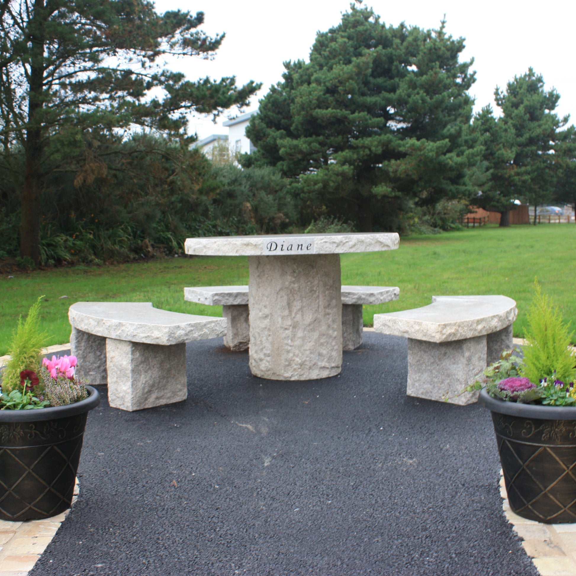 Garden with trees and Gold Granite Table & Bench Set on a tarmac area with two flower pots in the foreground. 