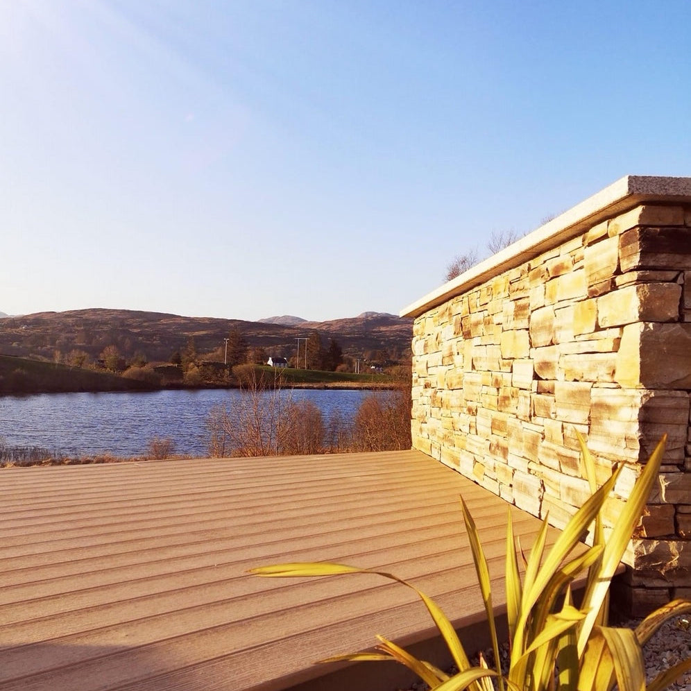 Wooden deck with stone wall overlooking a lake and mountains. Wall capping is Gold Granite. 