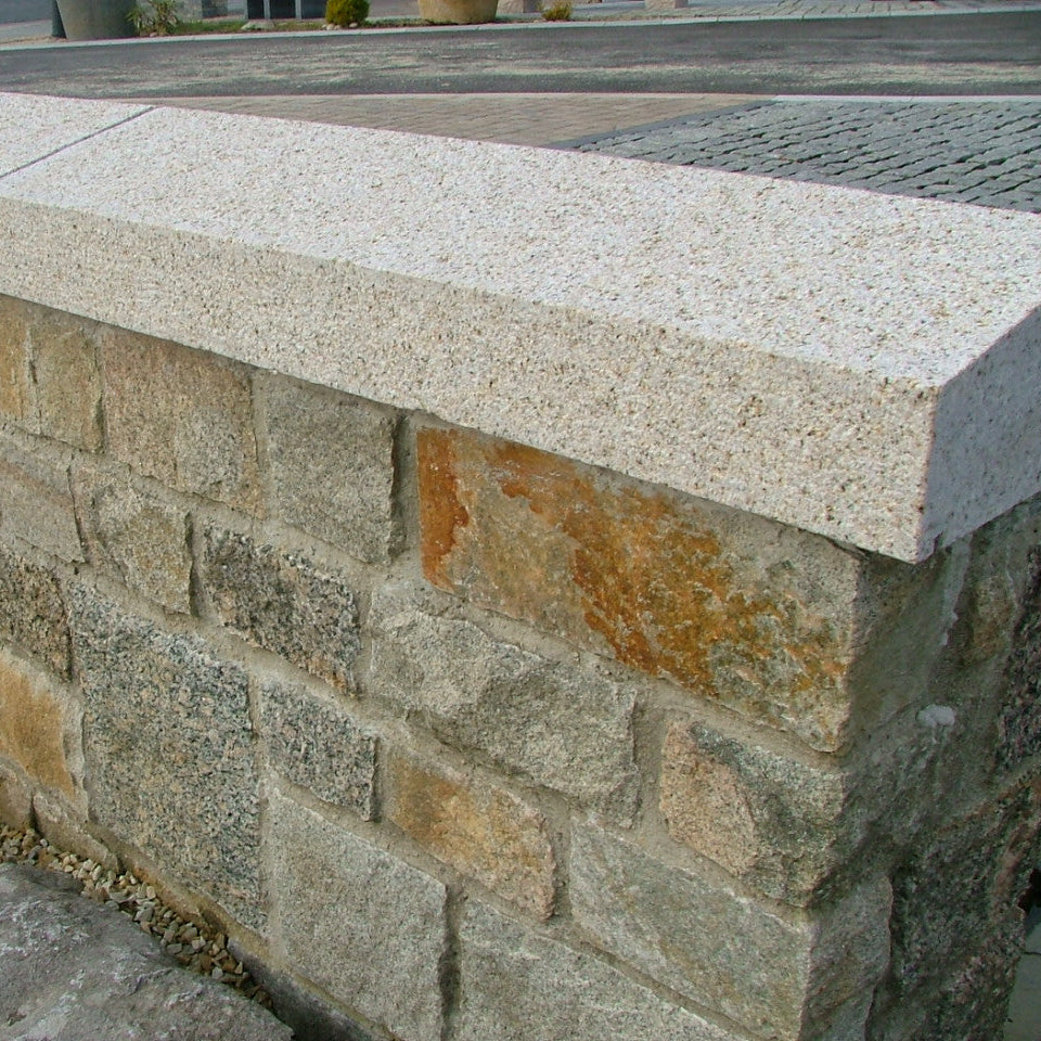 Stone wall with a gold granite wall cap in an outdoor setting. 