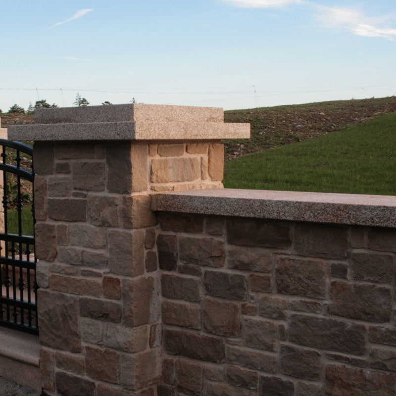 Stone wall with Gold Granite Wall Capping and a metal gate in a landscape setting.