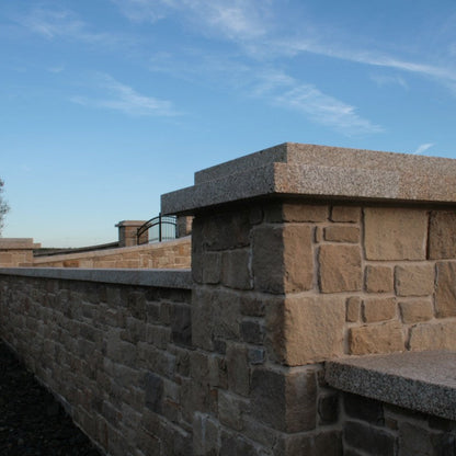 Stone wall with Gold Granite Wall Capping with a clear blue sky in the background.