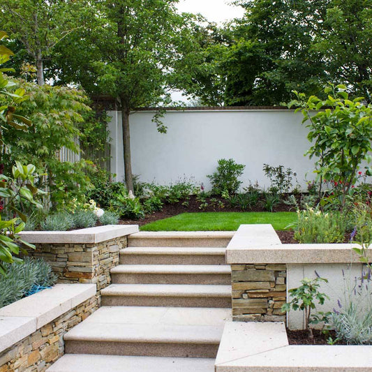 Garden with stone steps leading to a white wall with greenery. Garden walls completed using Gold Granite Wall Capping. 
