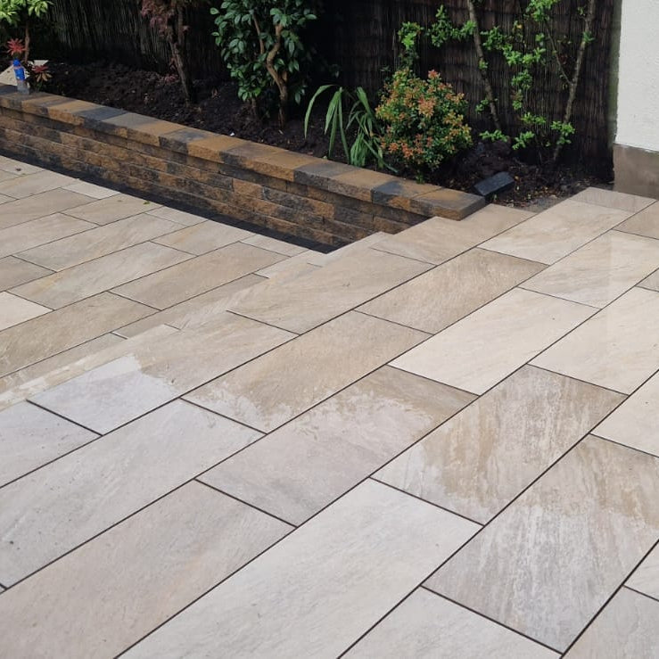 Paved patio area with stone tiles and a garden in the background. Paving is Gold Quartz Diva Range Porcelain Paving.  
