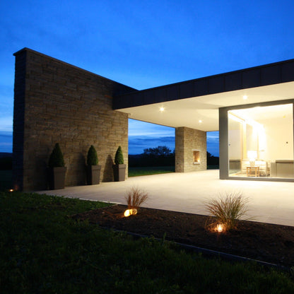 Modern house exterior with large glass windows at night. Stonework was completed using Grey Sandstone machined walling stone.