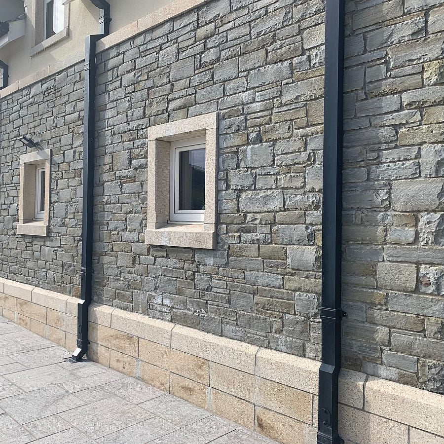External stone wall in grey sandstone machined walling and gold granite window surrounds, capping and plinth detail.