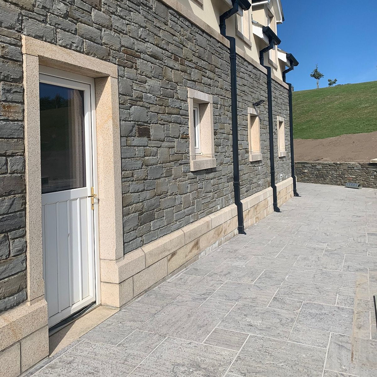 External stone wall in grey sandstone machined walling and gold granite door and window surrounds, capping and plinth detail.