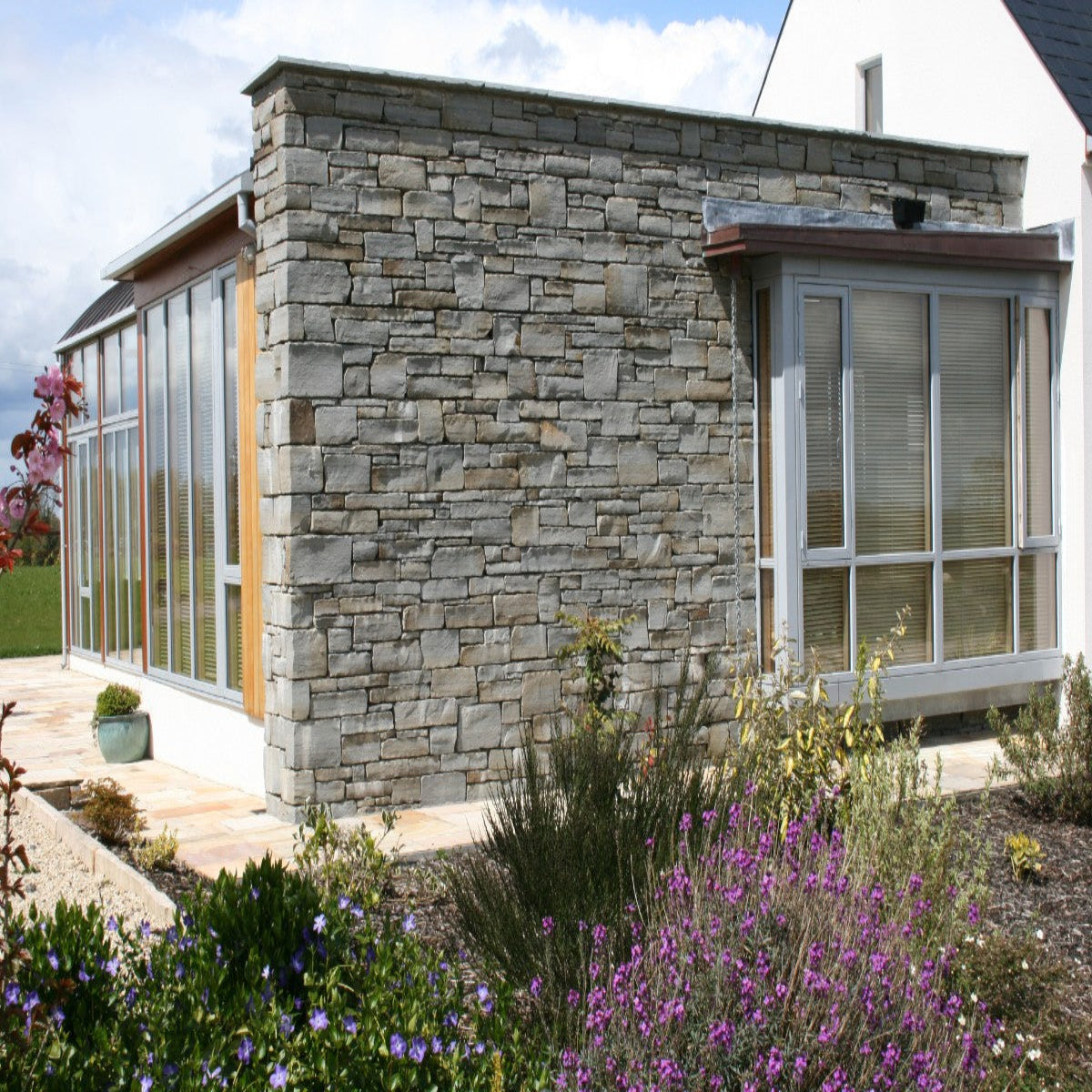 An exterior wall of a residential building featuring grey sandstone machined finish with large glass windows and a stone base.