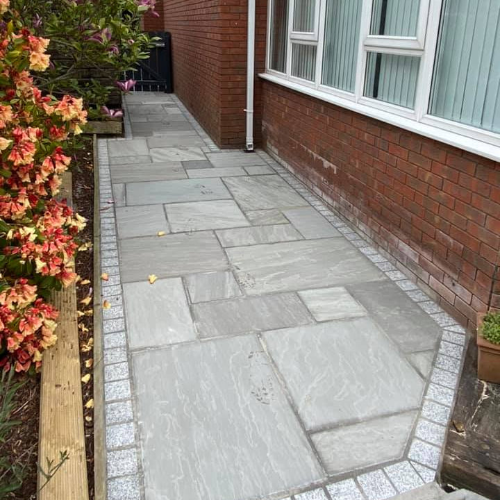 Pathway alongside a red brick house finished with Grey Sandstone Paving and Silver Granite Cobbles in 100 x 100mm size. 