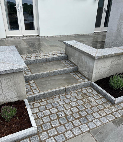 Outdoor stone steps leading to a building entrance with a paved area completed using Grey Sandstone Paving and Silver Granite cobbles. 